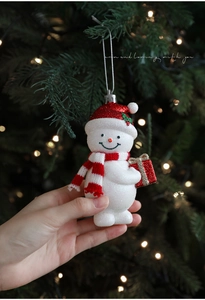 Close-up of glittery snowman ornament with red sequin hat and striped scarf on tree