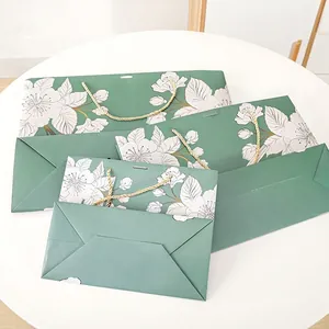 Elegant green paper gift bags with white floral patterns and gold braided rope handles