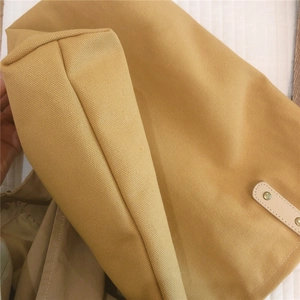 Detail of reinforced bottom seam and leather handle with metal rivet on yellow canvas tote