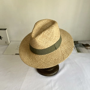 Detail of natural raffia straw hat with olive green grosgrain ribbon on wood base