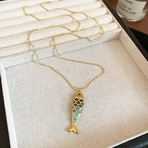 Detailed macro view of a golden fish pendant with blue-green enamel on a bead chain