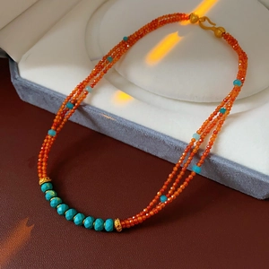 Detail of bohemian triple-layer orange beaded necklace with turquoise stones and gold spacers
