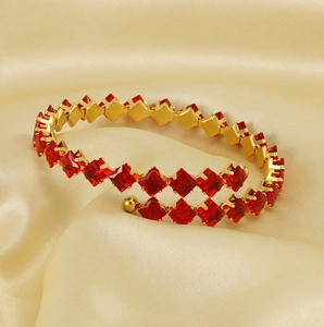 Macro detail of gold-plated bracelet featuring square-cut red zircon stones on silk