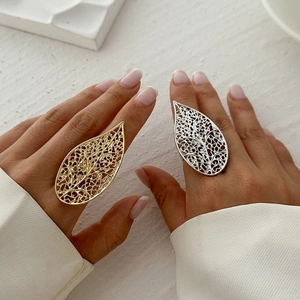 Close-up of golden and silver hollow leaf rings worn on a model's index finger