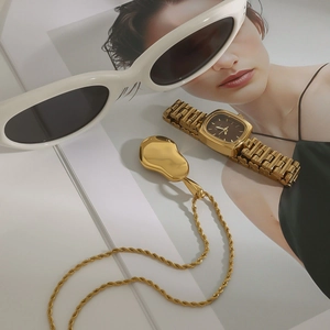 Flat lay of gold bean pendant necklace with textured chain and fashion accessories