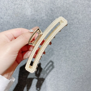 Détail de la pince à cheveux rectangulaire dorée ornée de perles blanches tenue à la main