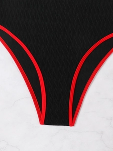 Close-up of black one-piece swimsuit featuring red trim and wavy textured fabric detail