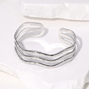 Minimalist silver wavy stainless steel open cuff bracelet on white textured stone