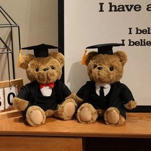 Brown graduation teddy bears with black academic gowns and yellow tassel caps on wooden desk