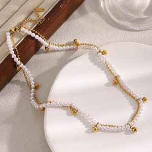 Détail d'un collier double rang avec perles blanches et pendentif doré sur plateau blanc