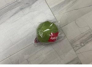 Detailed view of a green knitted Christmas ball ornament with red tag in clear packaging