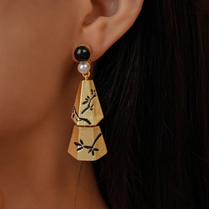 Golden geometric earrings with pearl accents and black bamboo leaf pattern on model