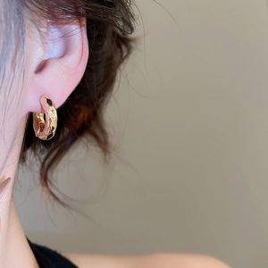 Close-up of a model wearing a gold resin hoop earring with a hammered texture finish