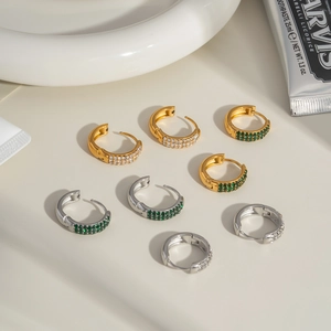 Close-up of gold and silver C-shaped earrings with zircon inlay on a white tray