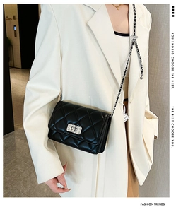 Detail of a black quilted chain bag with silver rectangular metal twist lock on a white suit
