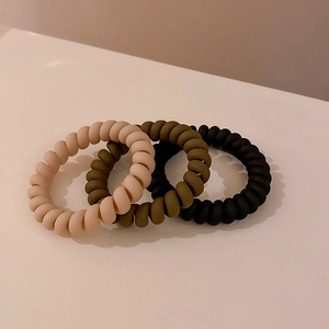 Detailed macro view of three matte spiral hair ties in beige, olive green, and black