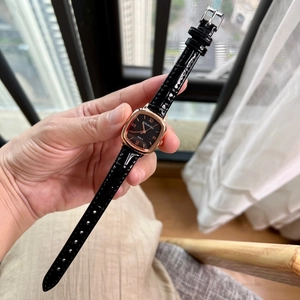 Square rose gold watch with black leather strap and Roman numerals held in hand