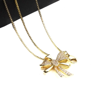 Close-up of golden bow pendant with micro-paved zircons on a delicate box chain