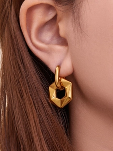 Close-up of a model wearing minimalist golden hexagonal drop earrings with metallic finish
