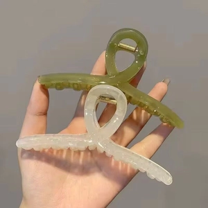 Detail view of two large hair claws in avocado green and cream white with gold metal spring