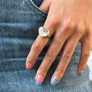 Close-up of a large heart-shaped crystal ring in gold finish worn on a finger