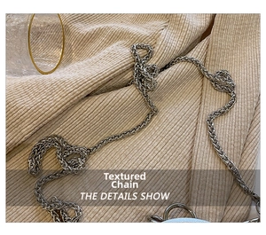 Detail of silver woven metal chain strap on textured beige fabric background