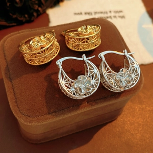 Detailed view of gold and silver hollow flower hoop earrings on brown velvet box