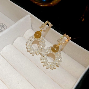 Detailed close-up of crystal pearl drop earrings on a beige velvet jewelry box