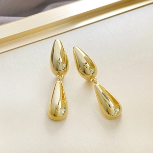 Macro shot of gold teardrop earrings with high-gloss finish on a beige textured background