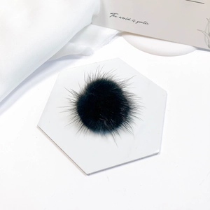 Close-up of soft black mink fur pompom accessory on a minimalist marble background