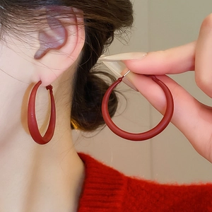 Detail of red matte C-shaped hoop earring on model showing minimalist geometric style