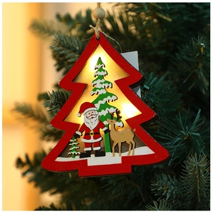 Close-up of a lit wooden Christmas tree ornament with Santa and reindeer on a pine branch