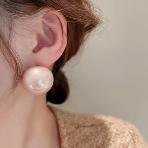 Dettaglio di orecchino a perno con perla rosa oversize su lobo di modella con ago argento