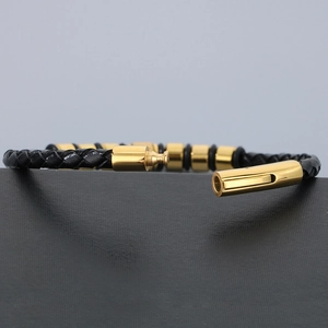 Detail of black braided leather bracelet featuring polished gold-plated metal cylinders