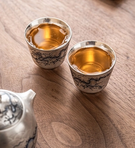 Detalle de las tazas de té de plata con patrón de dragón sobre una mesa de madera rústica
