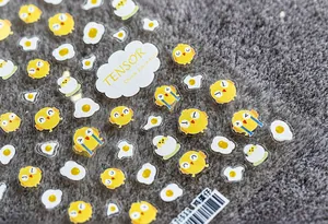 Détail des stickers ongles 5D motif poussin et œuf sur un fond en peluche gris doux
