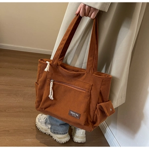 Side view of brown corduroy tote bag featuring front zipper and side pocket details
