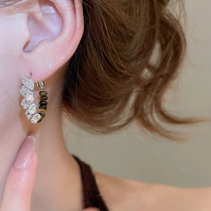 Close-up of C-shaped 18k gold earrings with tiger eye stone and zircon on model