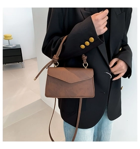 Détail d'un sac à bandoulière vintage marron avec poignée nouée et boucles métalliques dorées