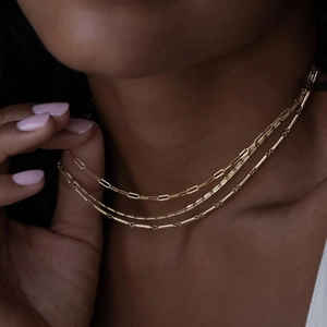 Layered gold necklace featuring paperclip and snake chains on a model with soft lighting