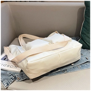 Detailed view of a white padded nylon tote bag with wide strap on a soft grey sofa