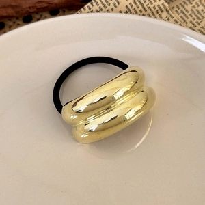 Detailed macro view of a glossy gold metal cuff hair tie on a minimalist ceramic plate