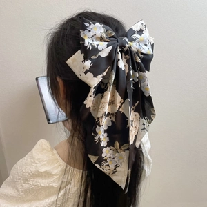 Detailed back view of a black floral satin bow hair clip with long ribbons on hair