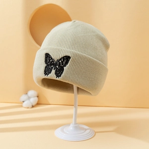 Beige ribbed knit beanie featuring black butterfly embroidery on a display stand