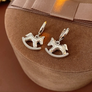 Close-up of silver rocking horse earrings with hammered texture on a brown velvet box