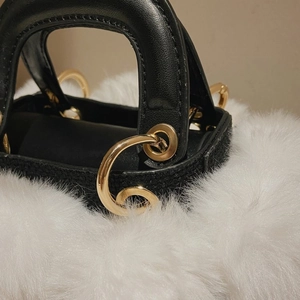 Close-up of black leather texture and white plush trim with a gold metal ring buckle