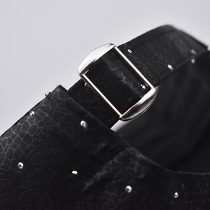 Detail of adjustable silver buckle and metal studs on black embossed baseball cap