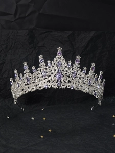 Detailed close-up of silver crown featuring purple crystals on black paper background