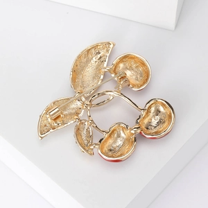 Elegant gold cherry brooch with red enamel fruits and detailed leaves on a white podium