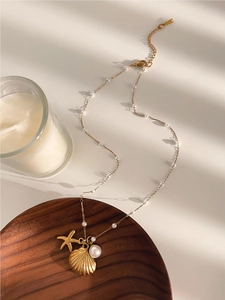 Detail of gold ocean necklace with starfish, seashell pendants and white pearls on a table